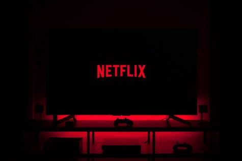 A dark screen shows the red Netflix logo. The background of the screen is illuminated by a red LED light.